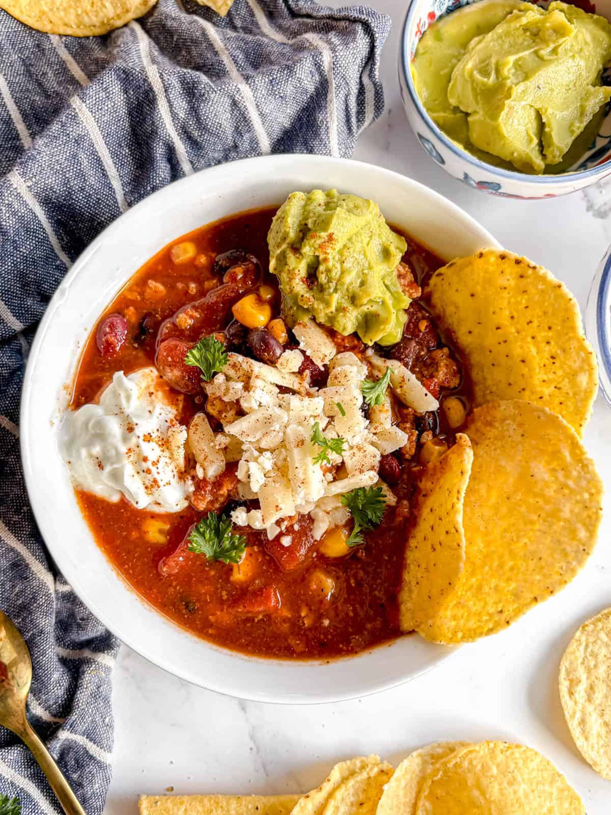 Crockpot turkey chili in a bowl with guac, cheese and greek yogurt on top.
