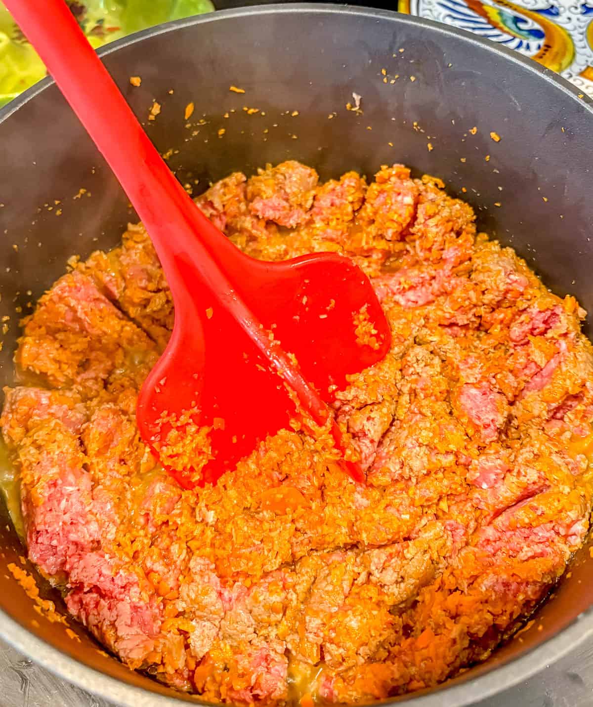 Using a meat masher to break up the beef.