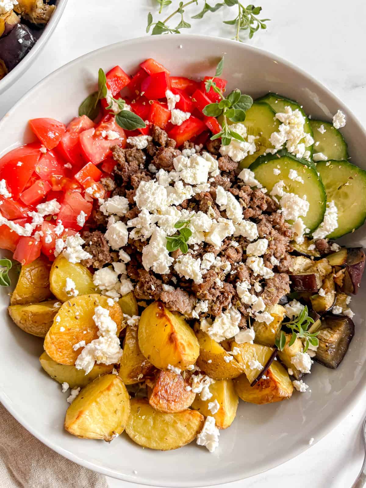 The greek bowls put together with potatoes, eggplant, cucumber, red pepper, tomato, ground beef, feta, oregano, and olive oil.