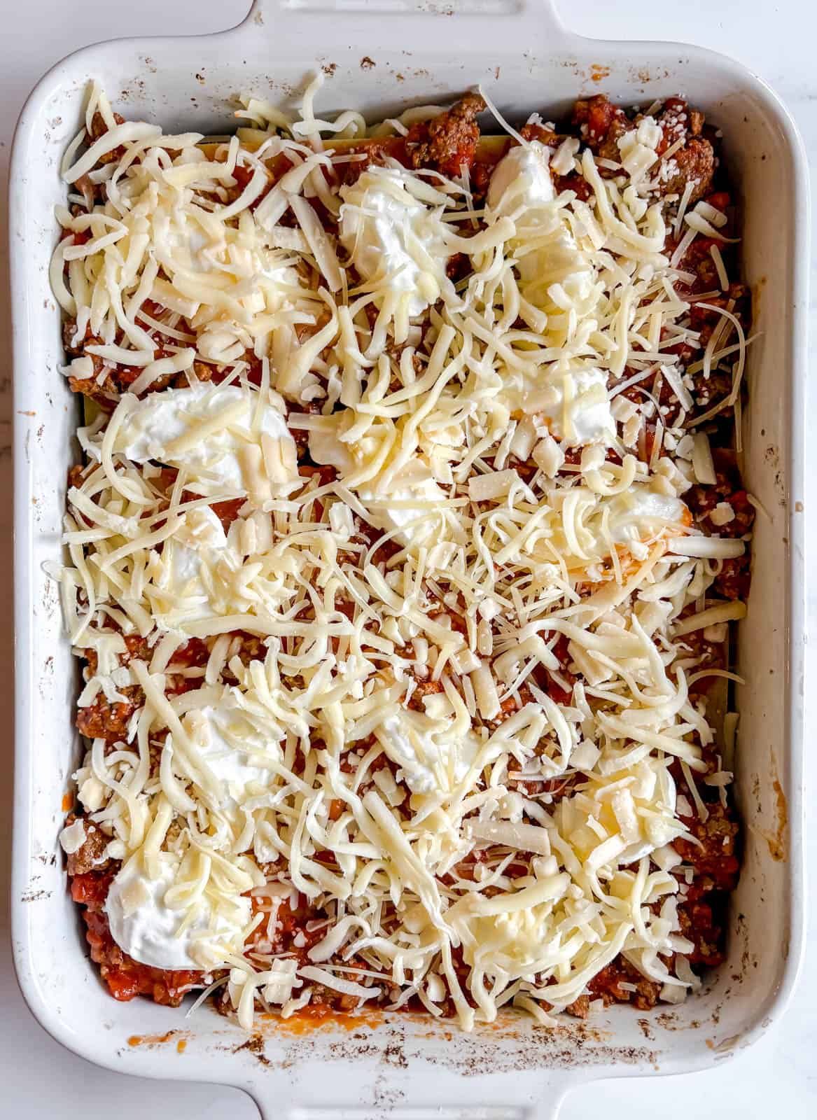 Greek yogurt and shredded cheese added to another layer of meat sauce in the lasagna.
