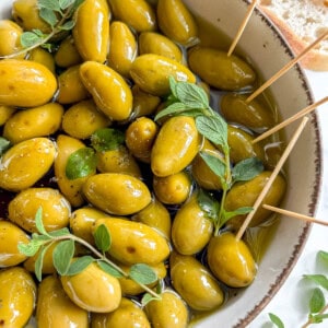 Warm Green Olives in Balsamic Vinegar and Olive oil in a bowl with toothpicks.