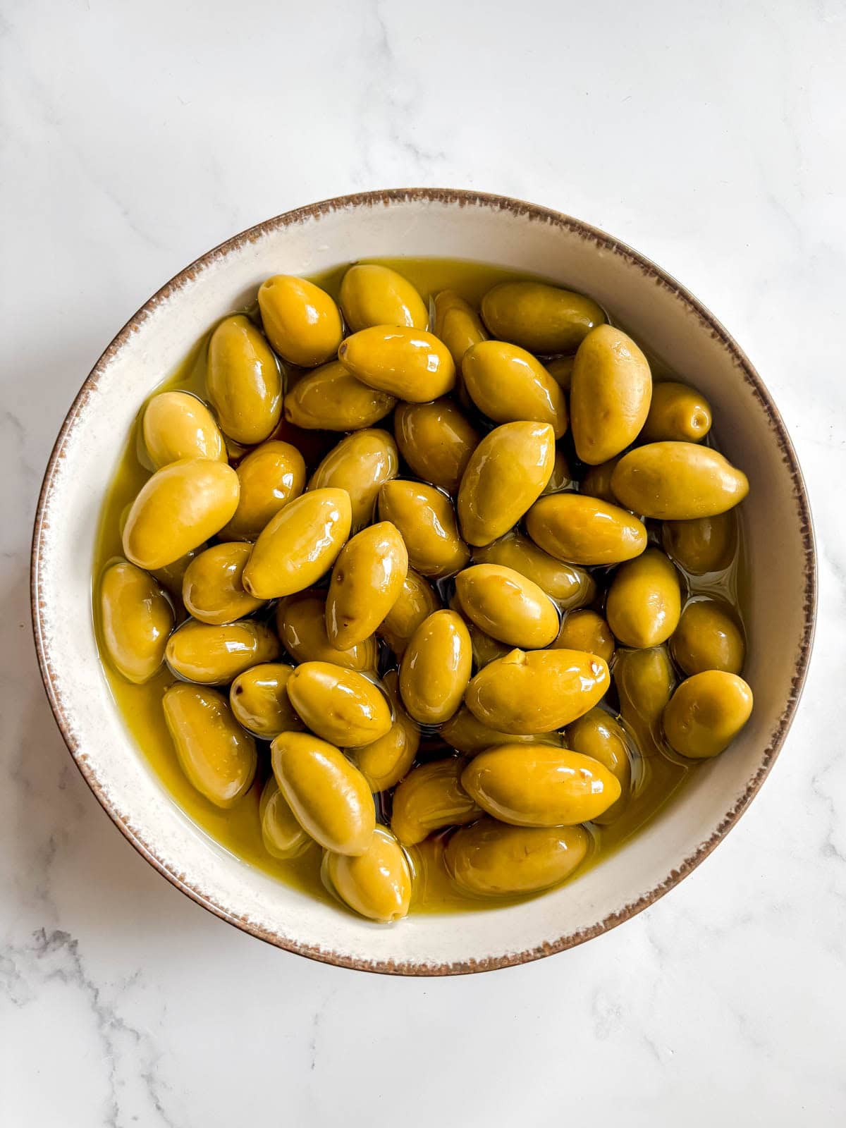 Green olives in a ceramic bowl with olive oil and balsamic vinegar on top.