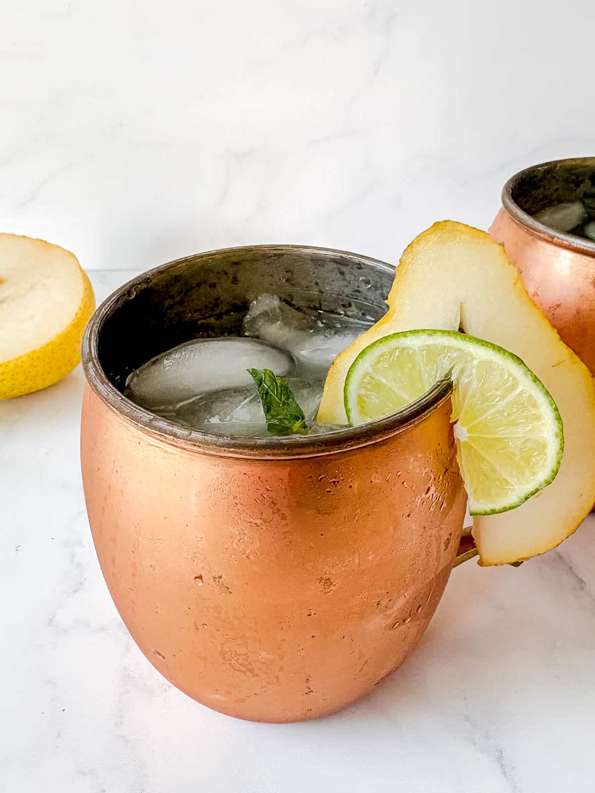 Pear Vodka Cocktail in a moscow mule cup with a sliced pear on the edge of the glass.