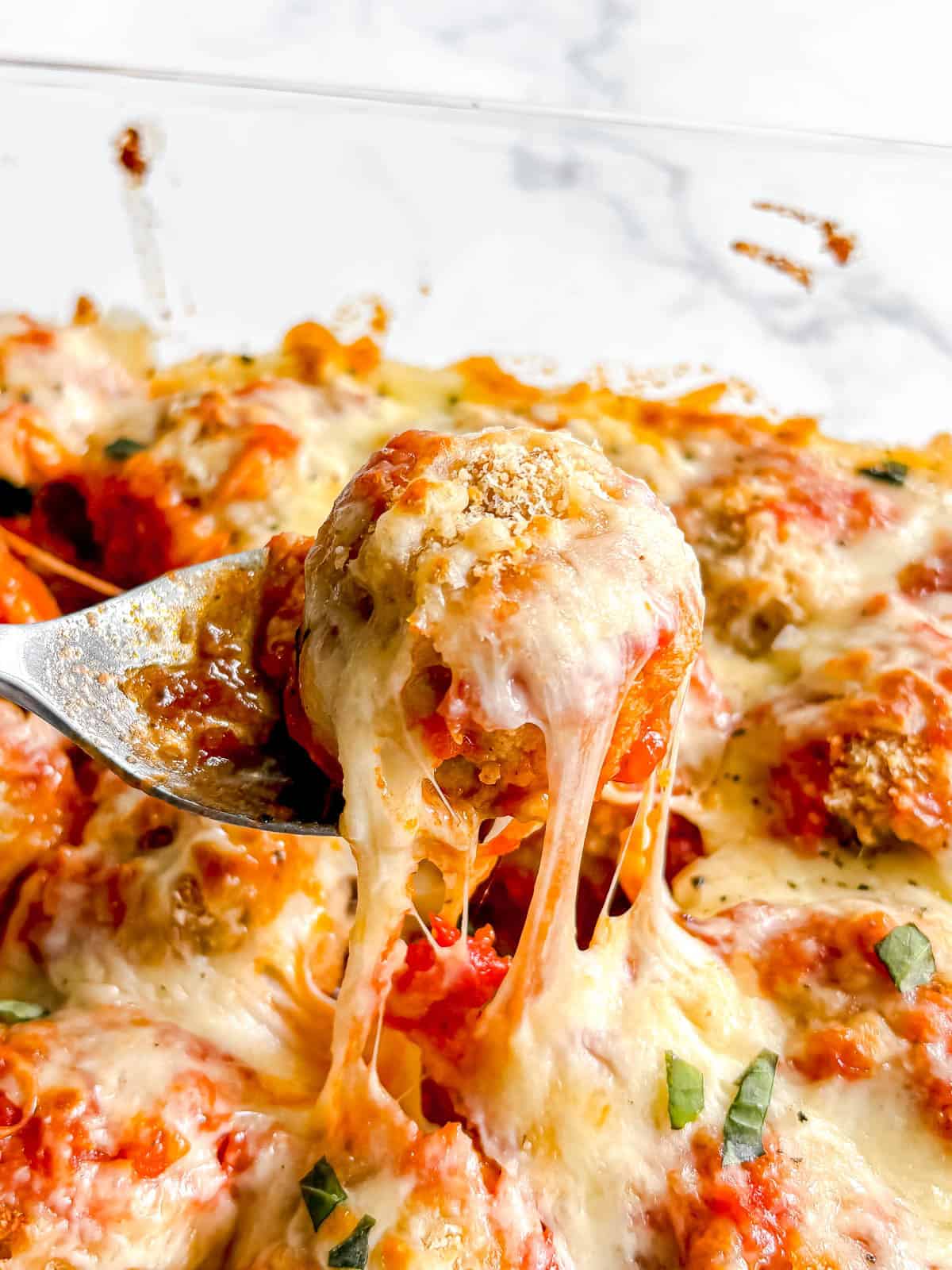 A gooey cheesy chicken parm meatball being lifted out of the dish.