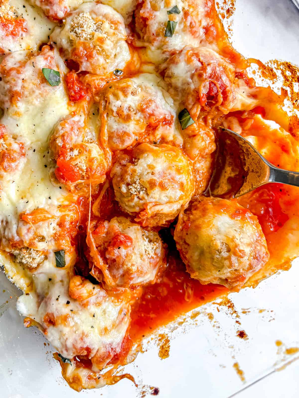 Chicken Parmesan Meatballs in a dish with a spoon reaching to spoon one out.