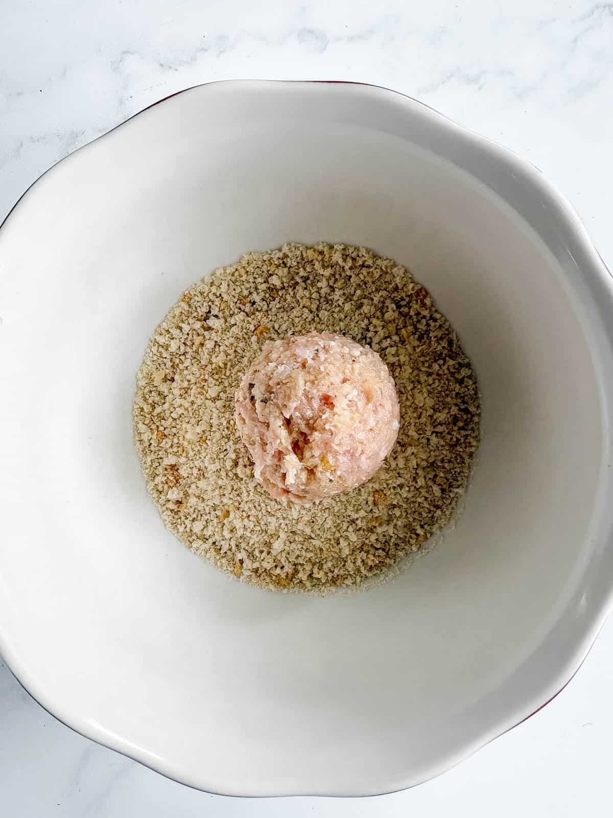 A chicken meatball in a bowl of breadcrumbs.