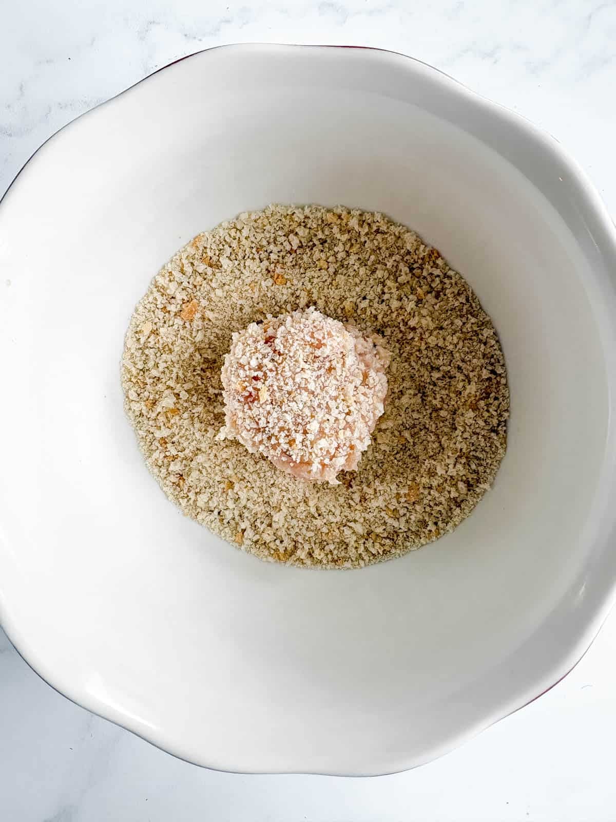 A chicken meatball rolled in a bowl of breadcrumbs.