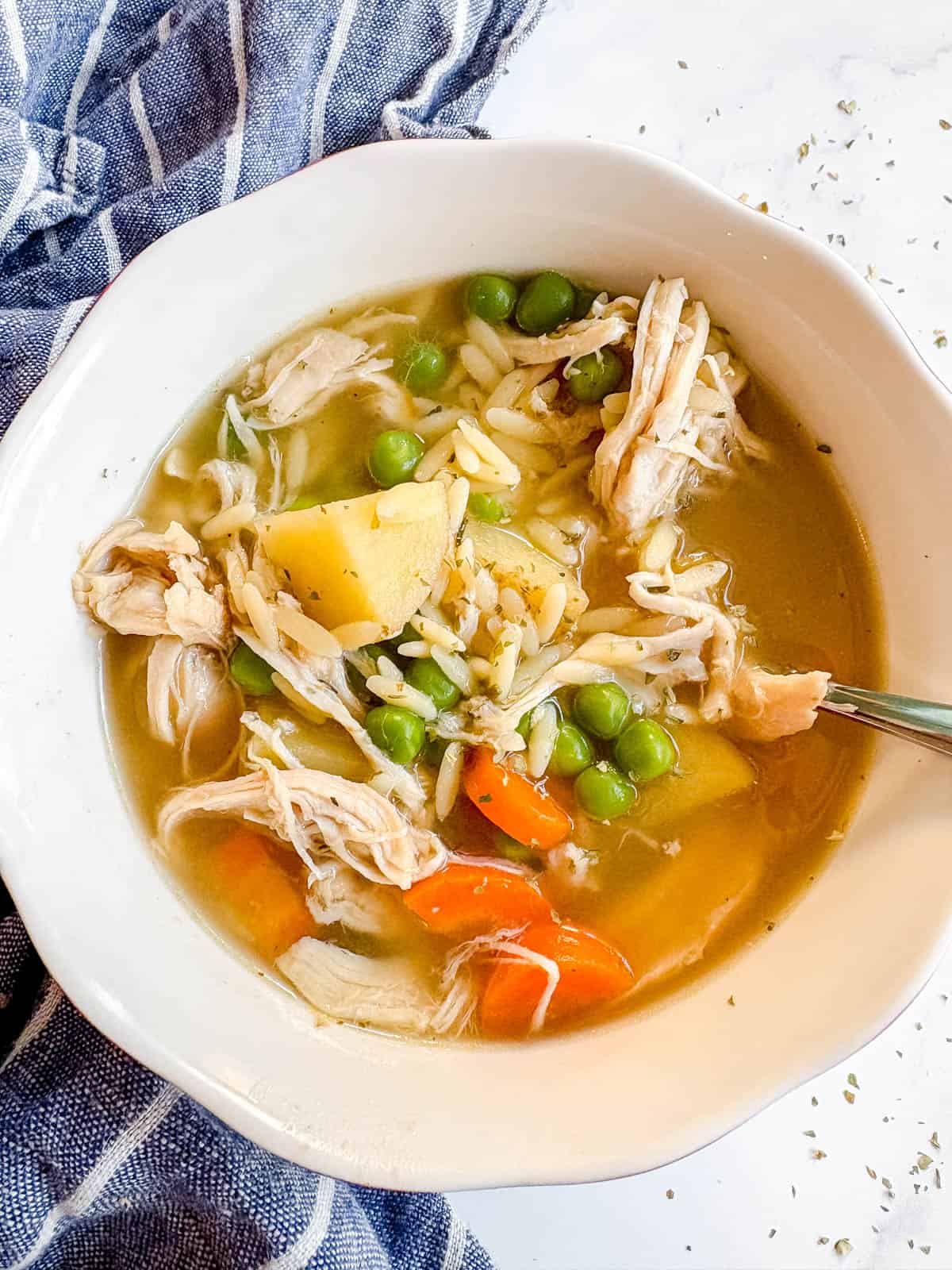 Chicken orzo soup in a bowl with a spoon in it.