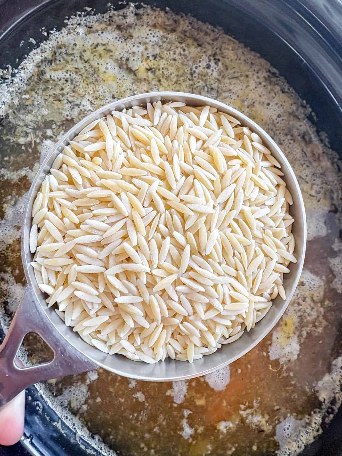 Orzo being added to slow cooker for chicken soup.