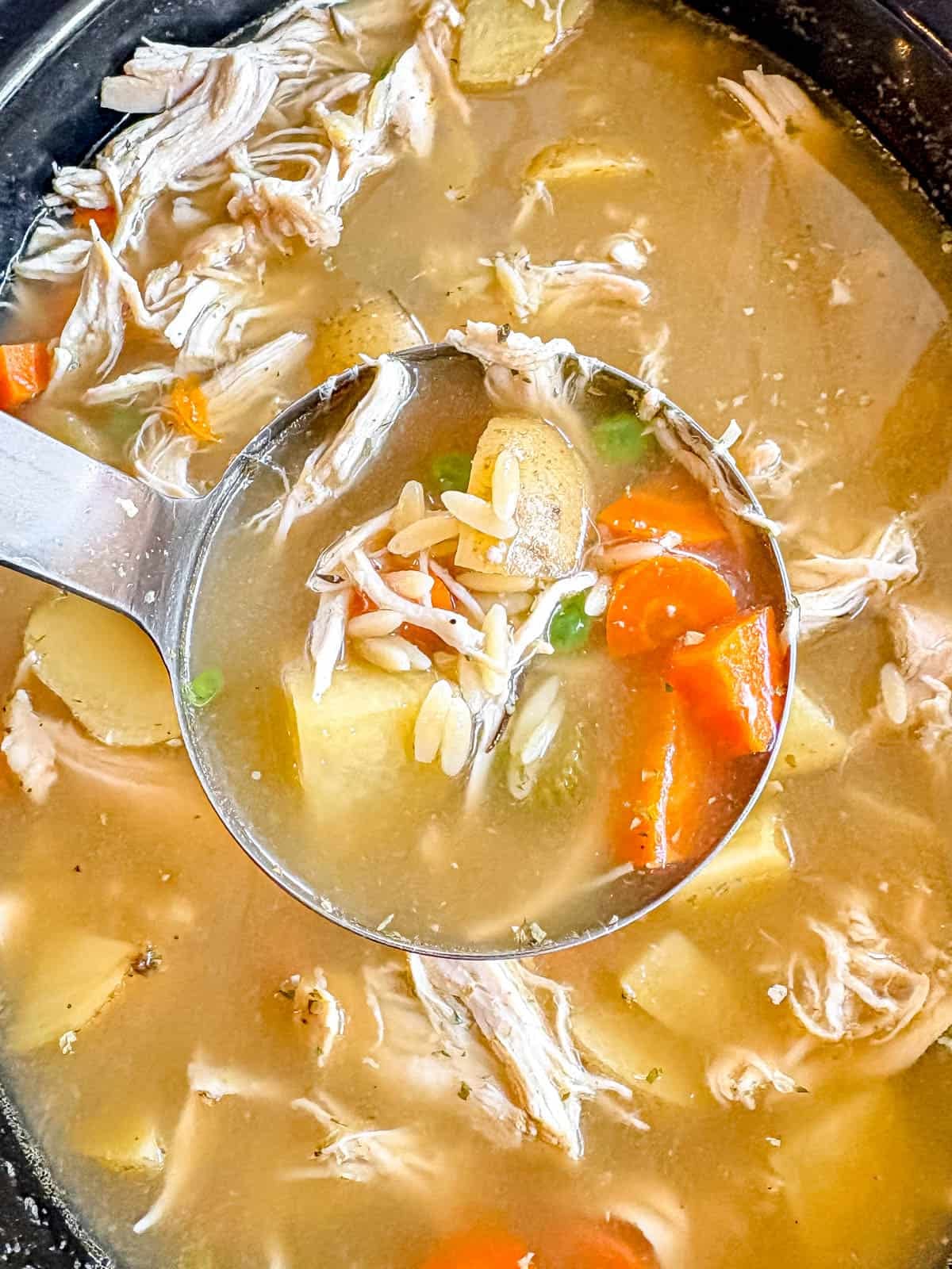 A spoon of crockpot chicken vegetable soup being lifted out of a slow cooker.